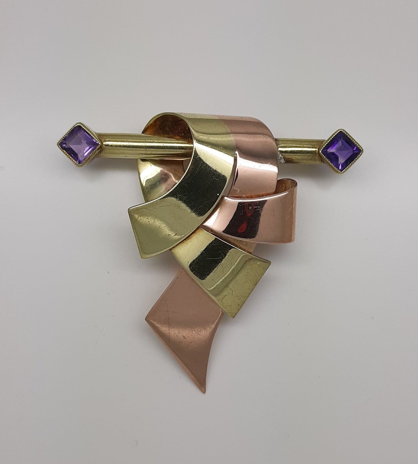 A lady's vintage Retro period 14k green and rose gold ribbon and bar brooch with square baguette cut natural amethyst accents.