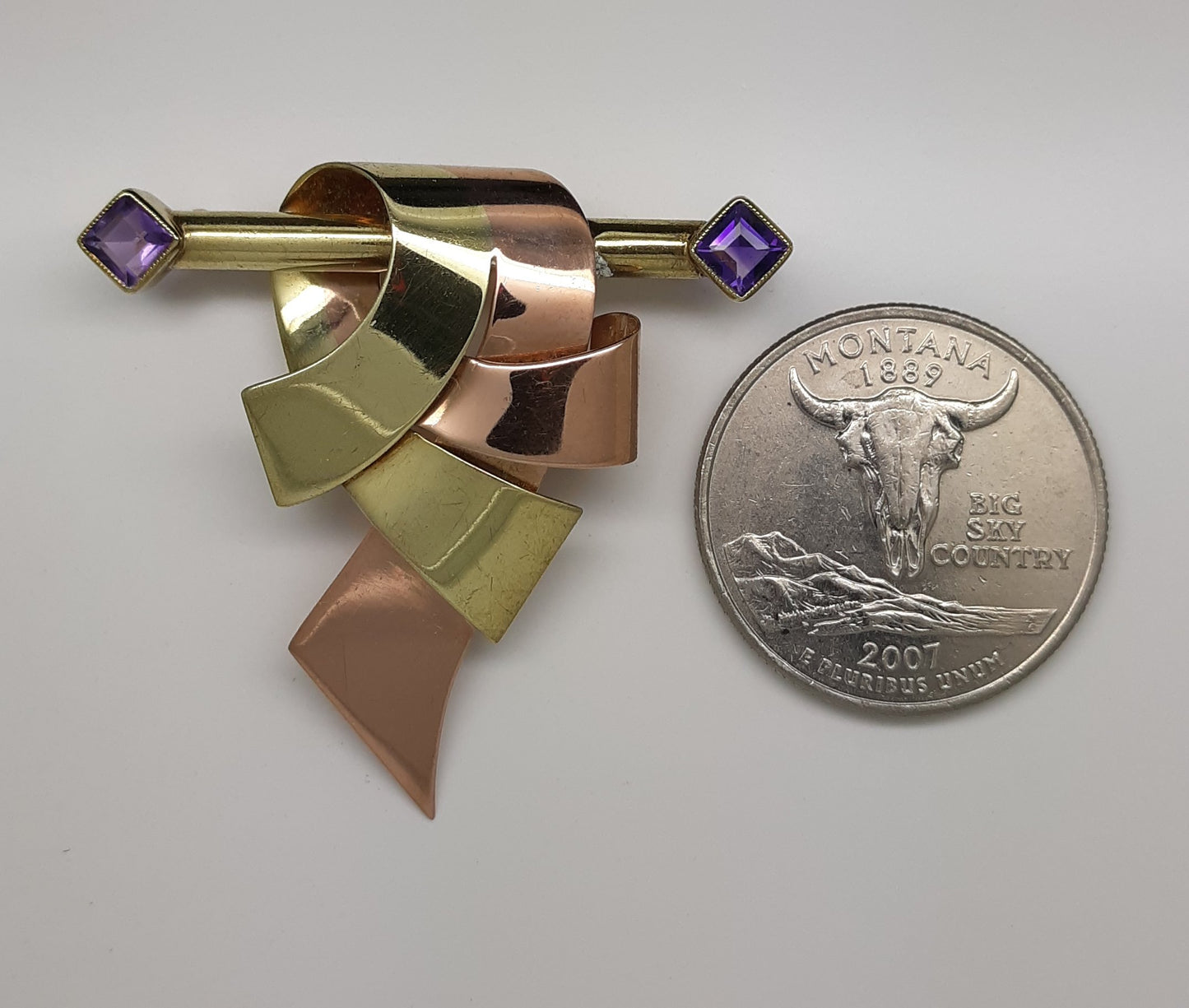 A lady's vintage Retro period 14k green and rose gold ribbon and bar brooch with square baguette cut natural amethyst accents.